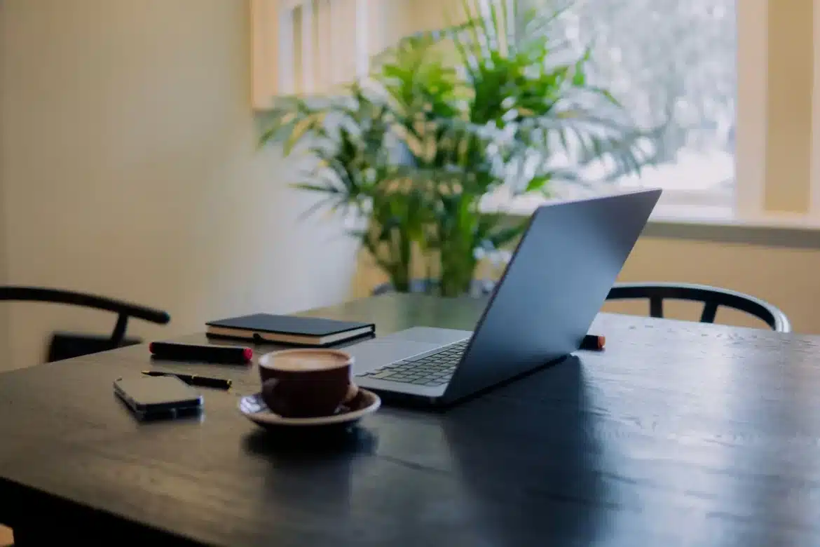 Personne à un bureau le matin, cahier et café, regard vers la fenêtre avec calme et détermination
