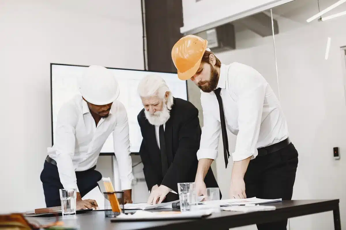 Équipe d'ingénieurs et de techniciens en réunion autour d'une table de travail dans un environnement industriel.