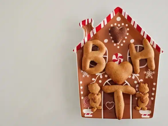 Mains assemblant une maison en pain d'épices avec du glaçage royal et des bonbons colorés