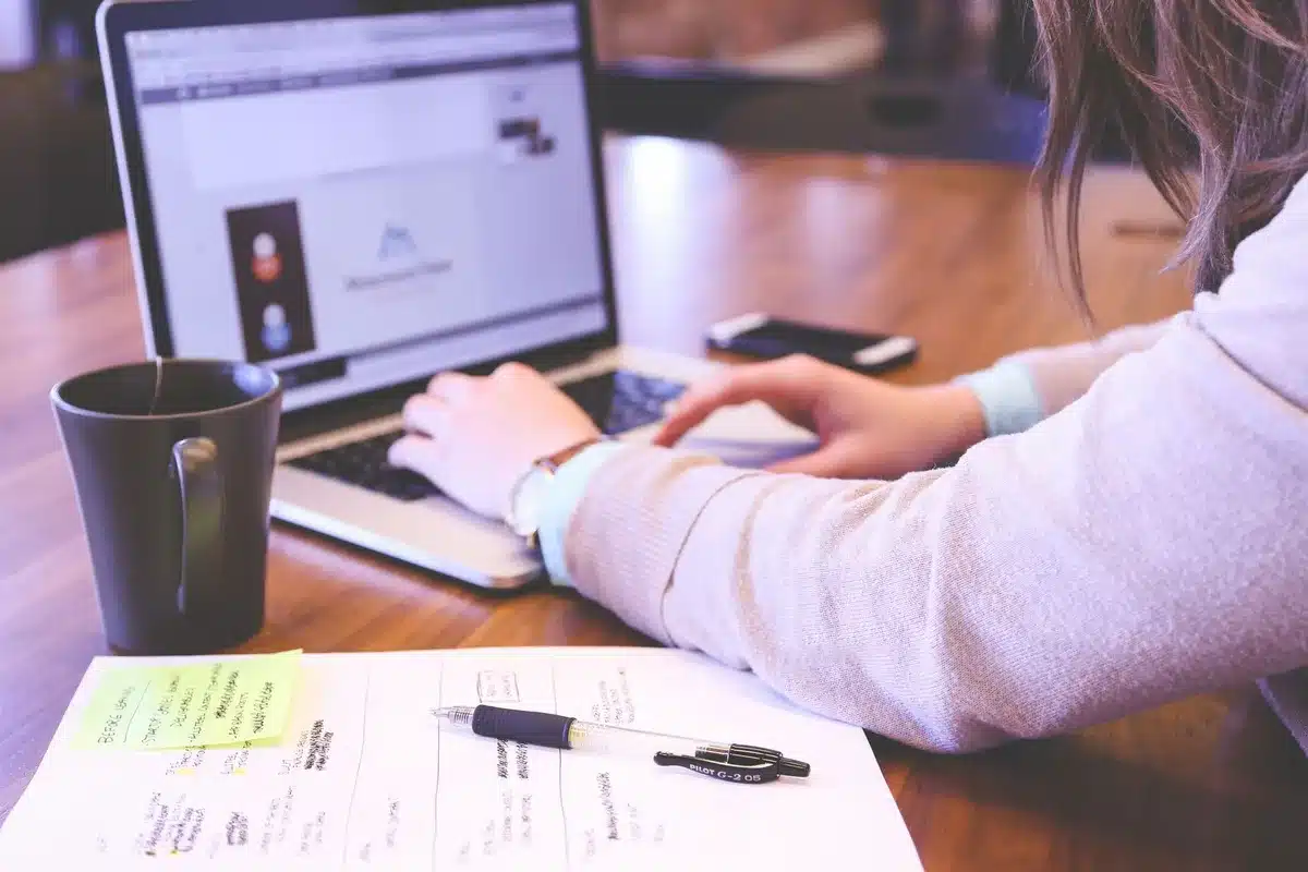 Freelance travaillant sur un ordinateur avec documents de tarification et prospection commerciale visibles