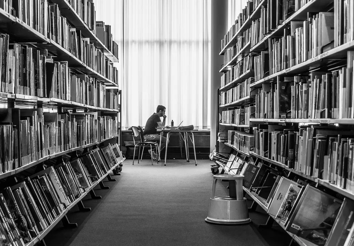 Main feuilletant une archive numérisée à l'écran avec des livres ouverts à côté