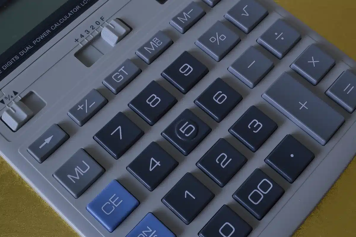 Personne comparant un tableau de budget avec une calculatrice près d'une fenêtre