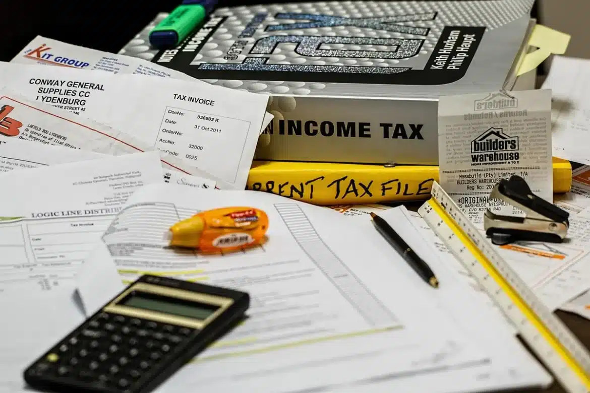 Bureau ensoleillé avec factures fiscales, calculatrice et ordinateur flou en arrière-plan